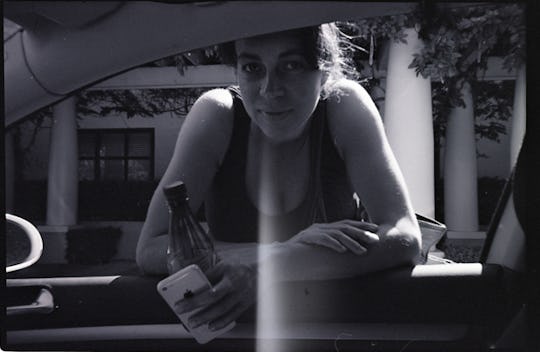 Woman leaning in car window with bottle and pack of cigarettes in hand