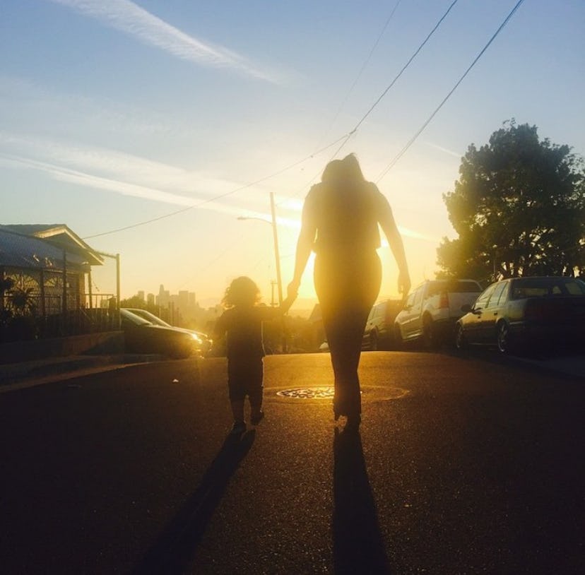 A mother holding her child's hand while walking during the sunset.