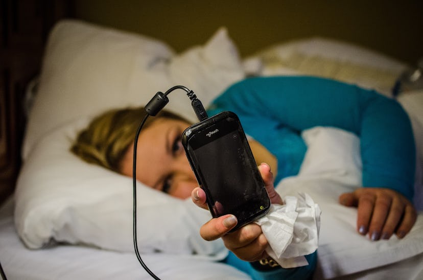 A blonde woman looking at her phone while lying in bed.