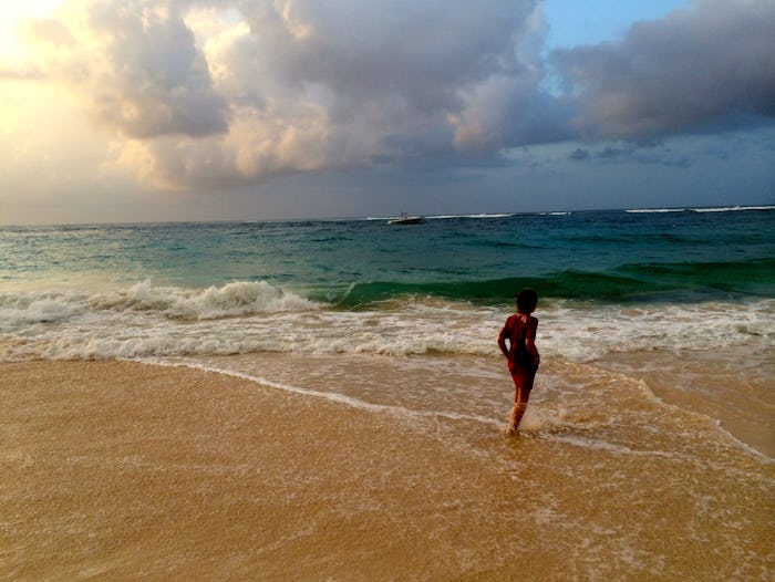 A woman in a red dress standing on a sandy beach in front of the waves.
