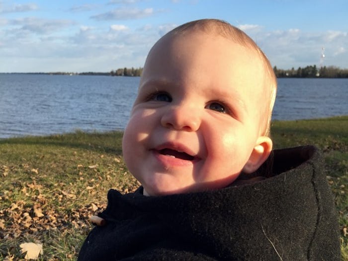 A blonde toddler smiling with the lake in his background