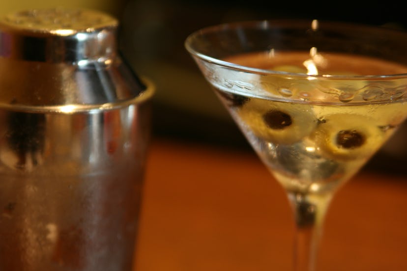 A glass of martini with two olives next to a cocktail shaker