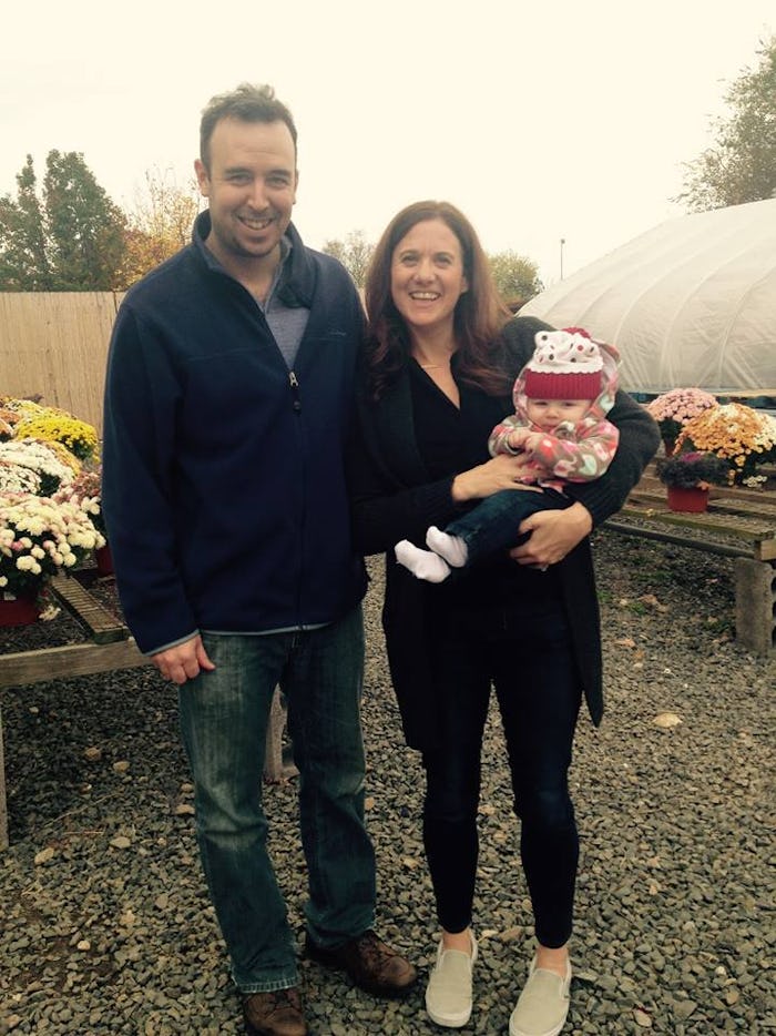 A working mom posing for a photo next to her husband while holding her baby