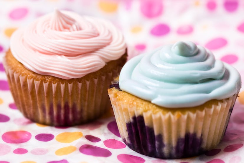 Two cupcakes, one with pink and the other with baby blue frosting on a purple polka dot paper.