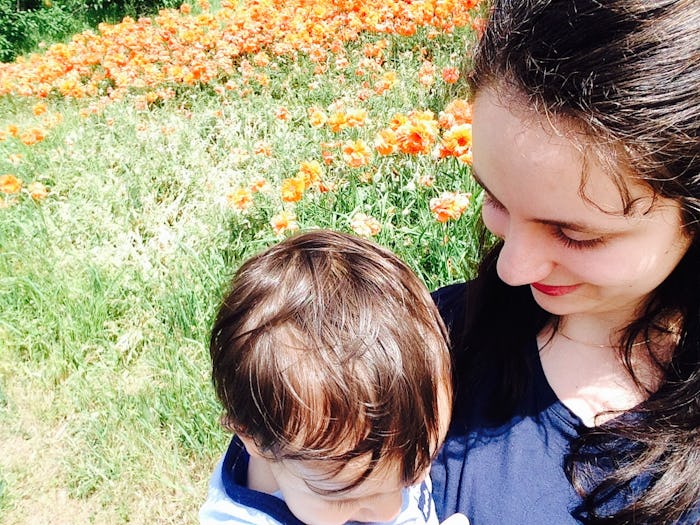 A mom holding her child while walking through a field of flowers on a sunny day