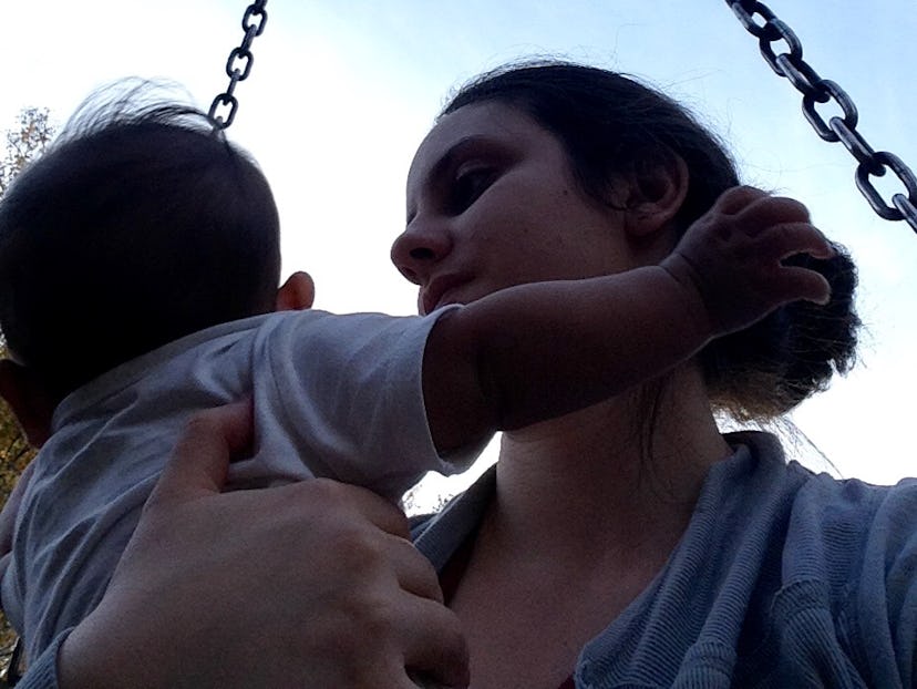 A woman is hugging her child, sitting on a swing on a sunny day. 