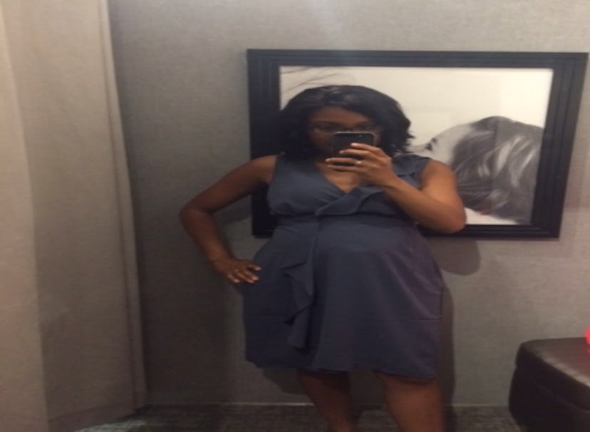 A black pregnant woman wearing a grey dress taking the picture of herself in the mirror