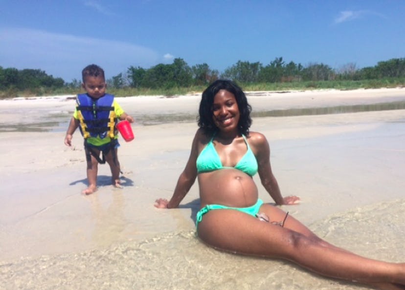 A pregnant black lady posing on the beach in a light blue bikini with her son