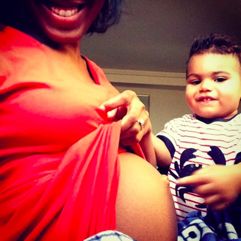 A pregnant woman showing off her stomach with her son touching it