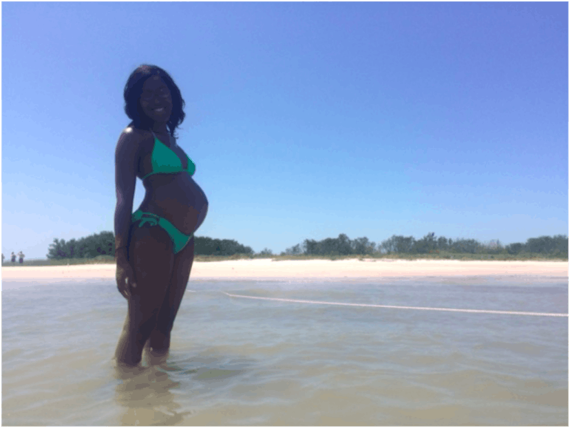 A pregnant woman wearing a light green bikini posing for the picture in the sea