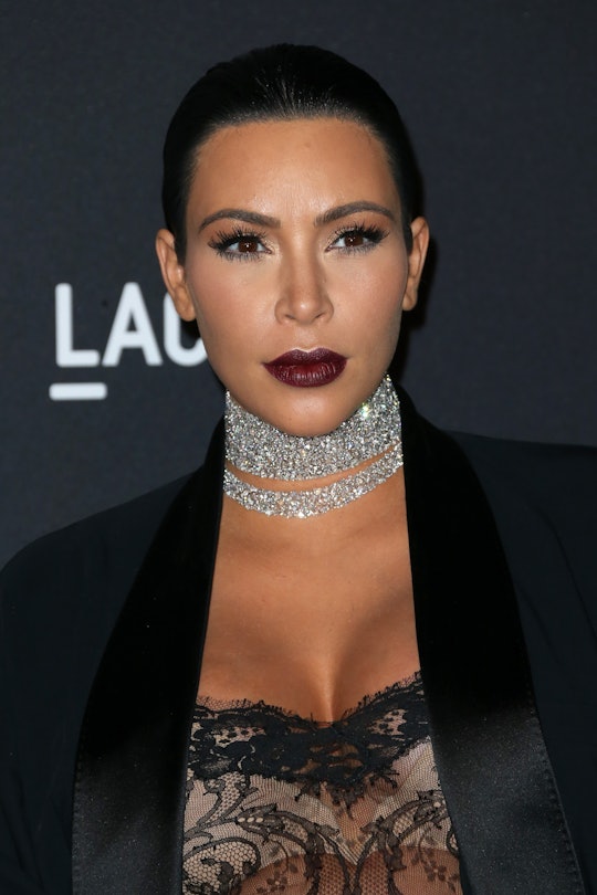 Kim Kardashian  in a blazer and lace dress with slicked back hair and a silver necklace at a red car...
