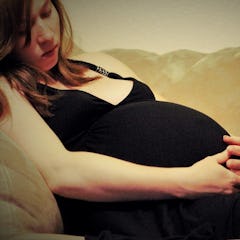 unhappy looking pregnant woman in black dress laying on couch holding base of her belly