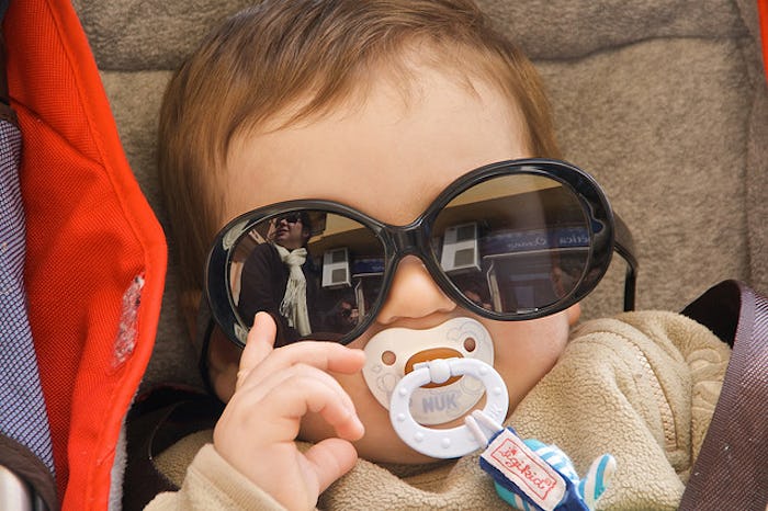 A badass baby posing with black sunglasses of its mother