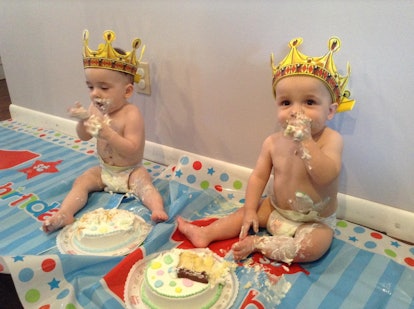 Twins wearing diapers and crowns on their heads while eating birthday  cakes