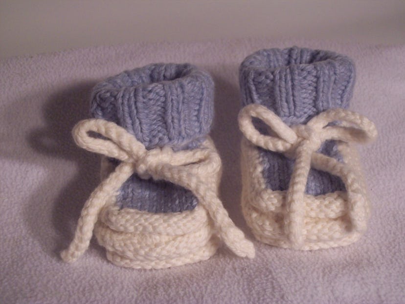 A pair of blue-knitted baby shoes with white shoe laces placed on a pink surface.