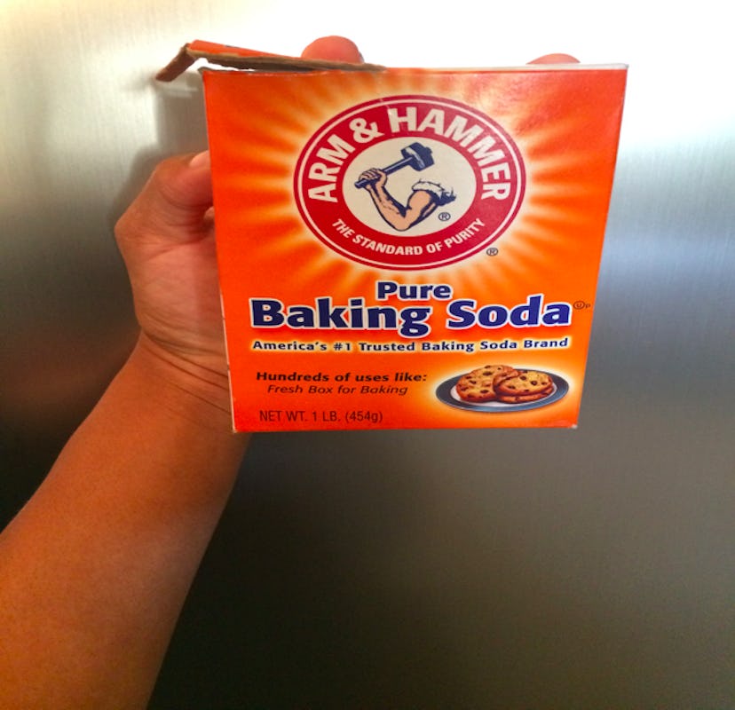 A hand holding an orange "Pure Baking Soda" box in front of the gray background.