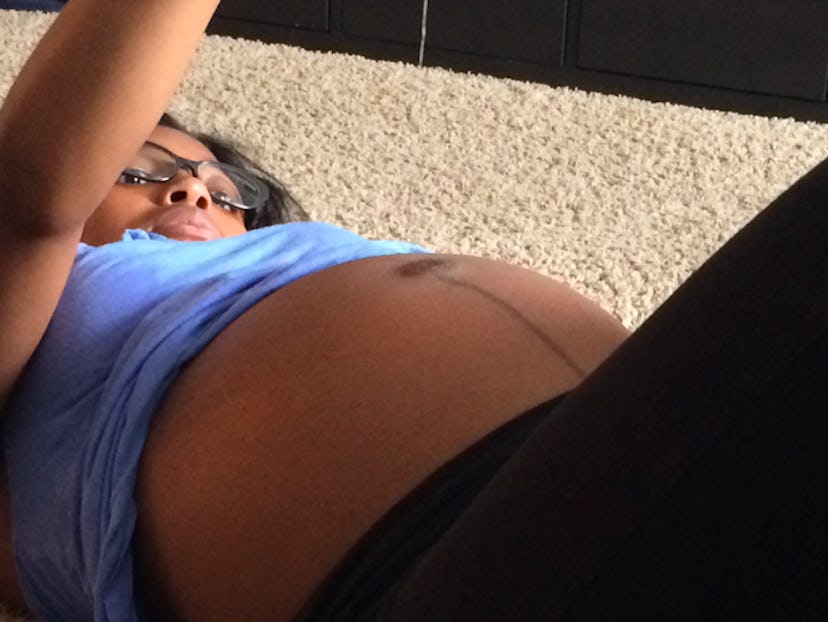 A pregnant woman with a blue top and black leggings is lying on the floor, holding a string above he...