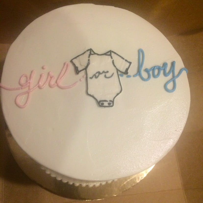 White cake with a "girl" written in pink frosting and a "boy" written in blue frosting with "or" wri...
