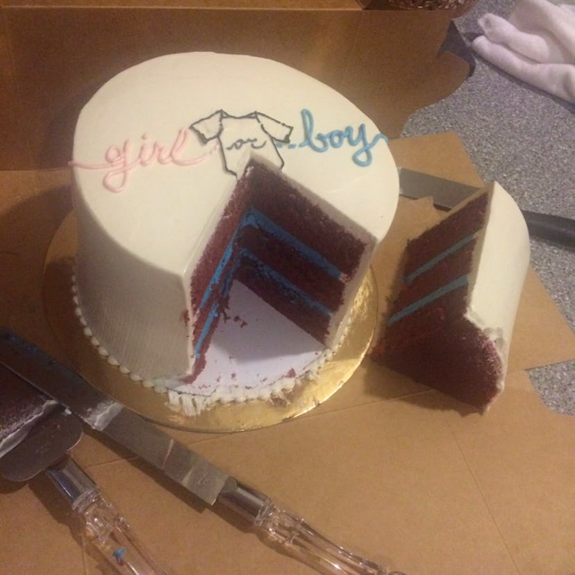 White cake with a piece cut out made out of blue frosting, indicating that the baby is a boy.