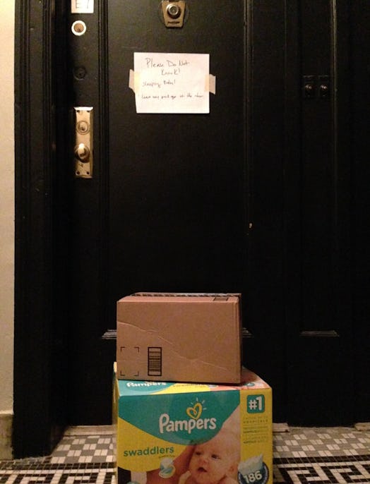 Two box packages in front of the door, one of them being the Pampers package, with the note taped on...