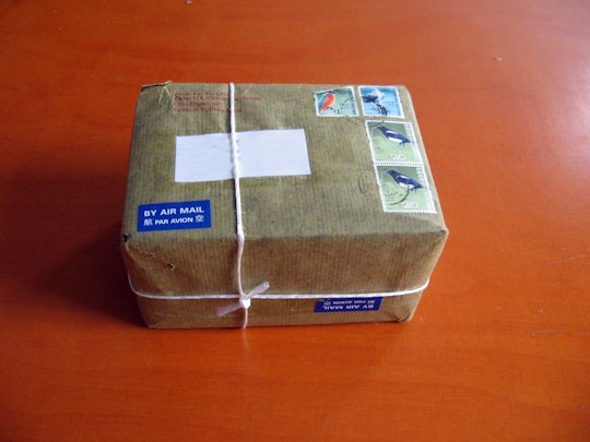 A package in brown packaging paper with various stamps on it tied with string on an orange table