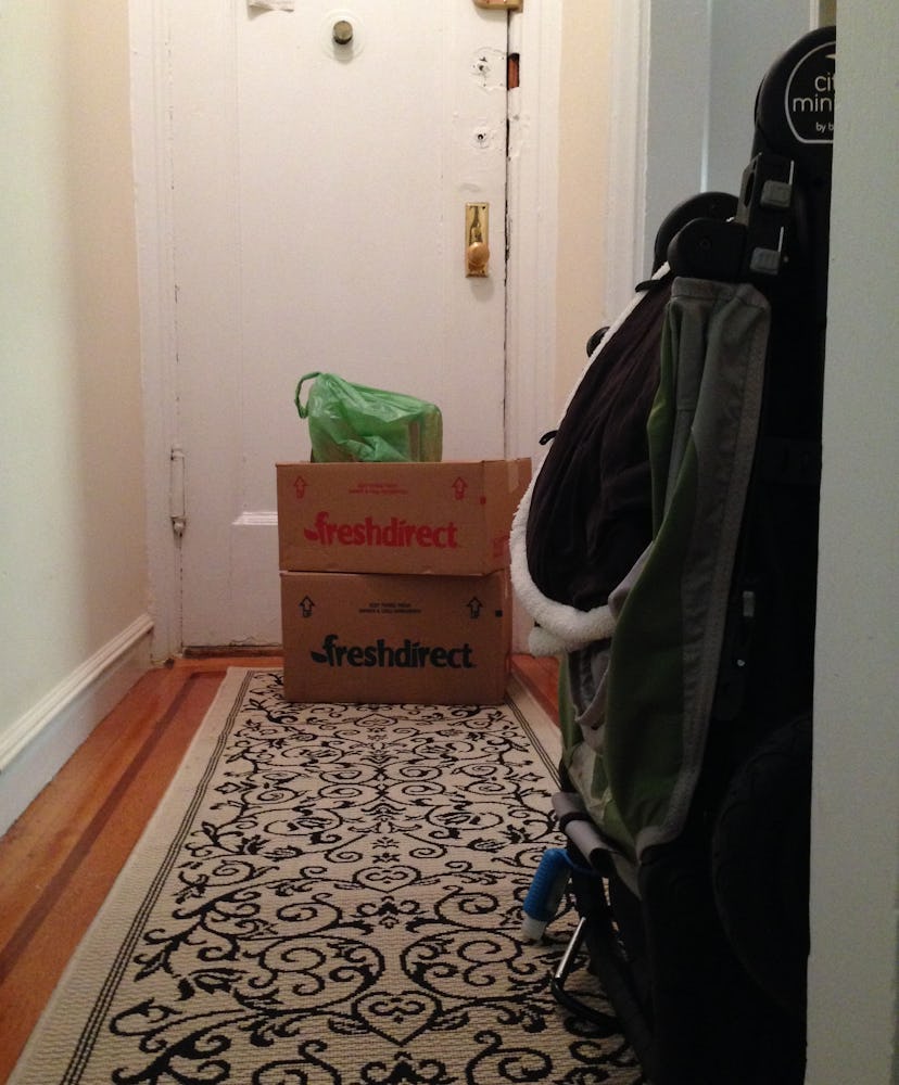 Two boxes stacked in front of the white door in a home hallway, with a green bag on top of them.