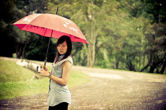 A woman posing for a photo during rain while holding a red umbrella