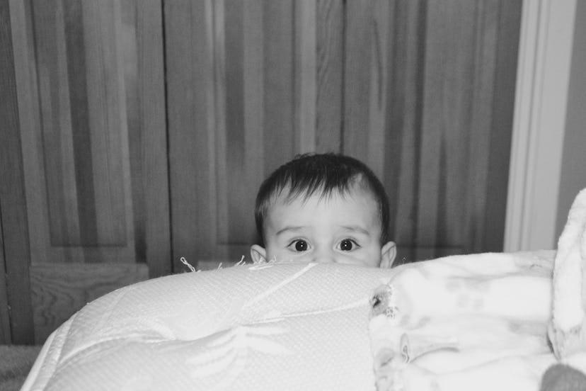Black and white picture of a baby peaking behind the bed.