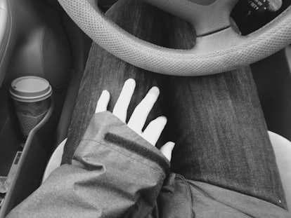 A woman sitting behind the wheel in a car with her hand on her thigh.