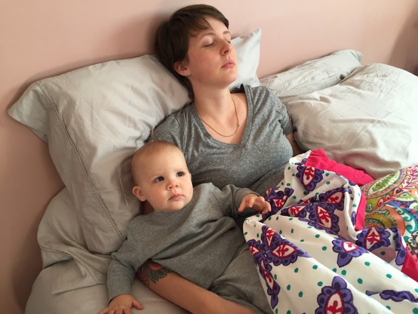 A mom and a baby girl lying in bed and wearing matching gray clothes.