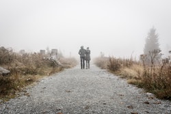 A couple with their arms around each other walking down a foggy desolate road