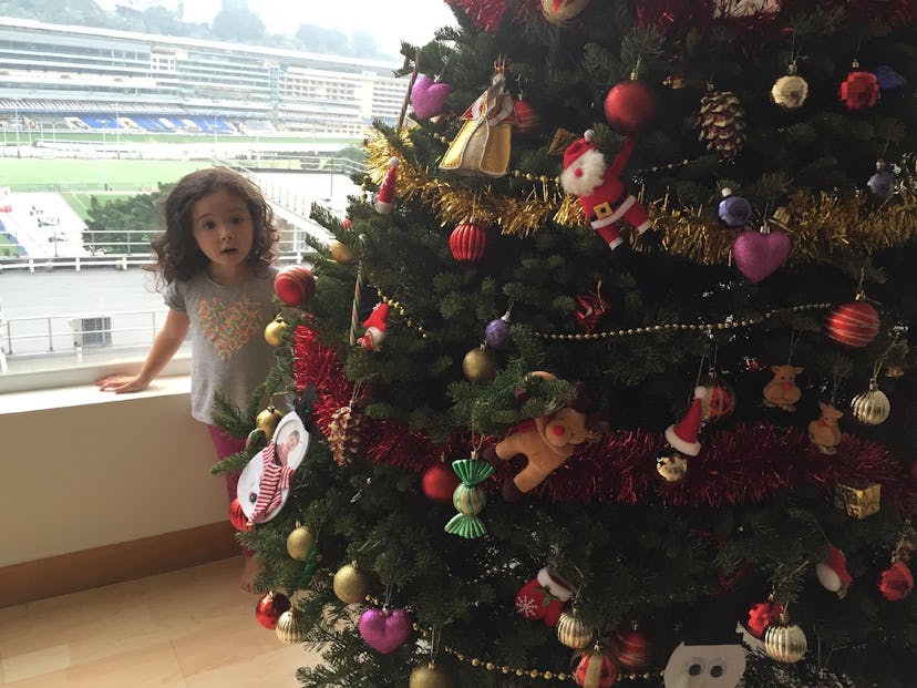 A little girl peeking behind the Christmas tree