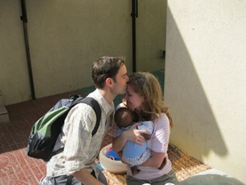 Lauren Casper holding a baby while her partner kisses her forehead.