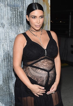 Kim Kardashian holding her pregnant belly while posing in a black sheer dress