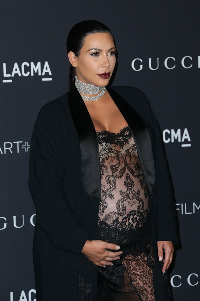 Kim Kardashian pregnant in a black lace dress, black coat, and diamond choker on a red carpet event