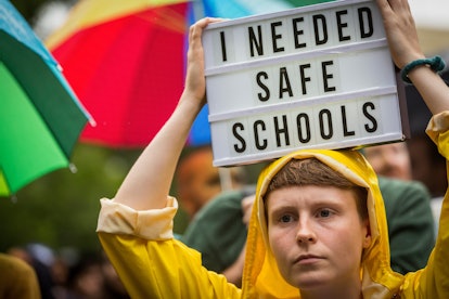 A woman holding a text sign with "I needed safe schools" text