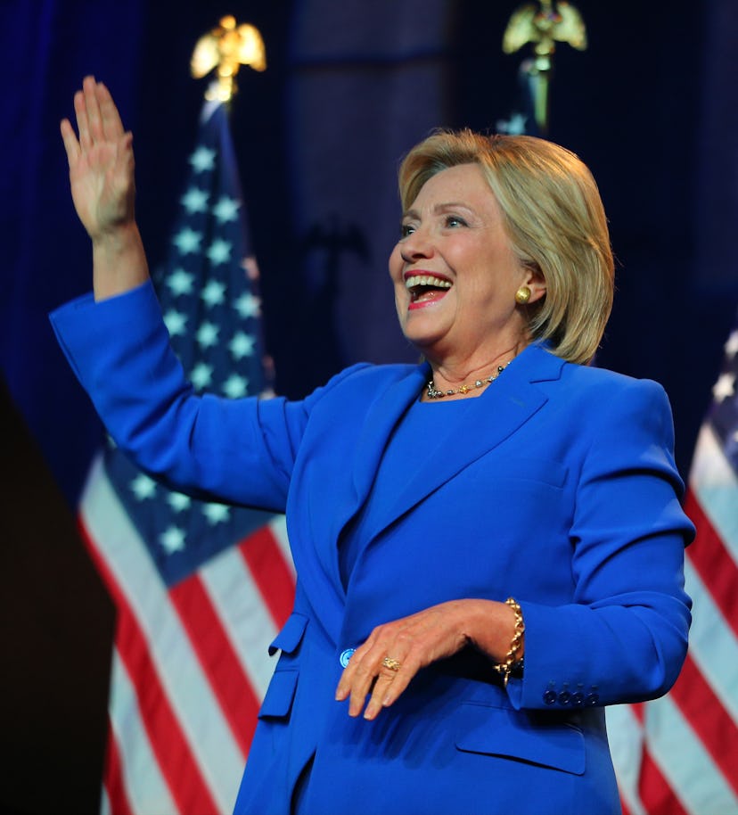 Hillary Clinton smiling and waving with her right hand in a blue suit