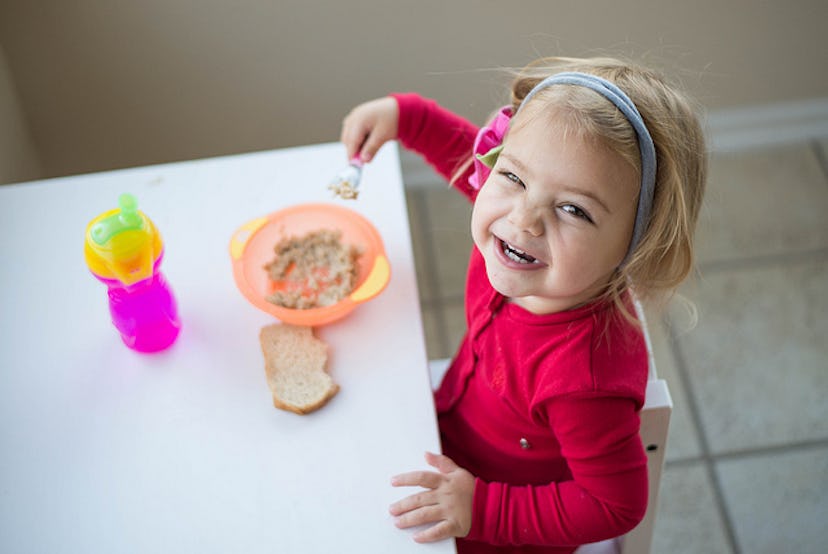 A small girl smiling and eating her meal alone