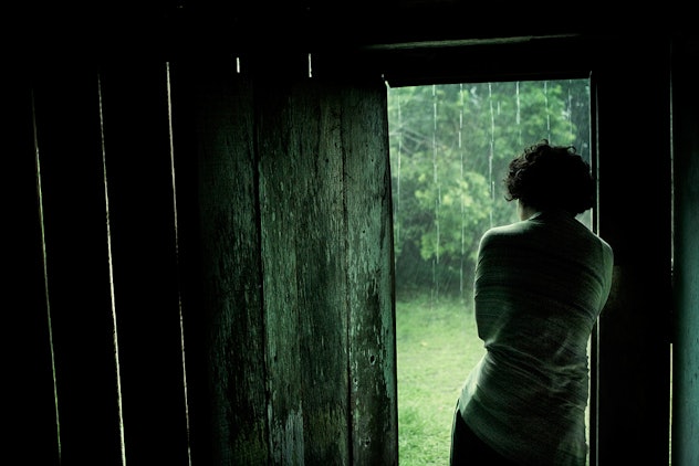 A woman standing on the wood cabin door and watching the rain outside