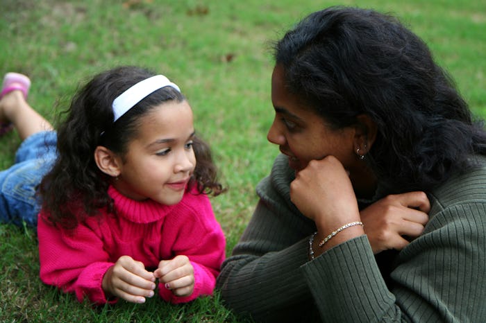 A woman and her daughter lying on their stomachs in the grass talking to each other.