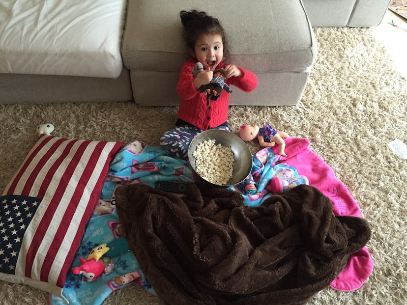 A little girl with a bowl of popcorns in front of her, playing with her toys on the floor 