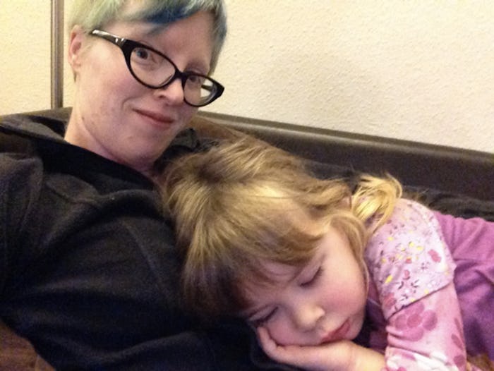 A mom with anxiety sits on a couch with her daughter lying on her