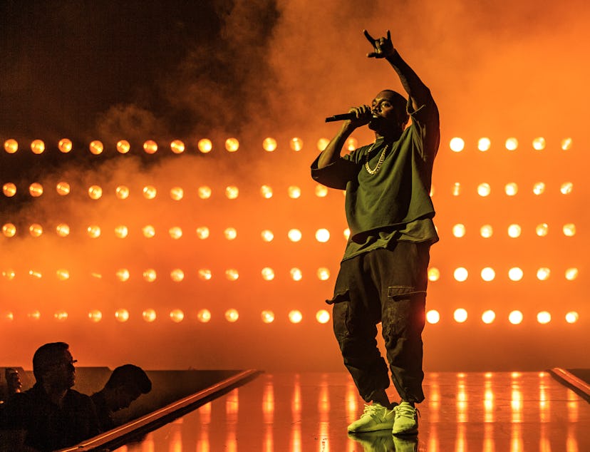 Kanye West performing on stage in a green top, black pants and green sneakers