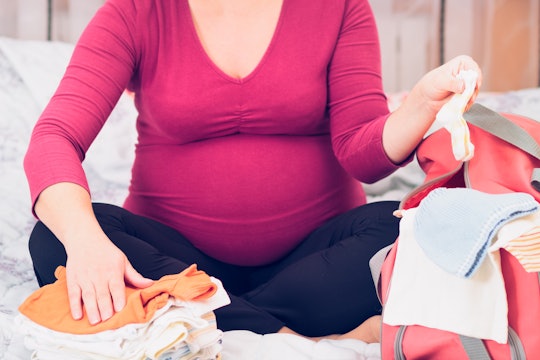 Pregnant woman sitting with her legs crossed packing her hospital bag