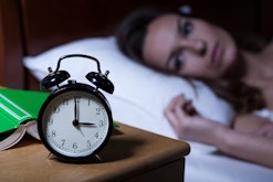 A woman who has insomnia lying in bed looking at her alarm clock, coping with the end of daylight sa...