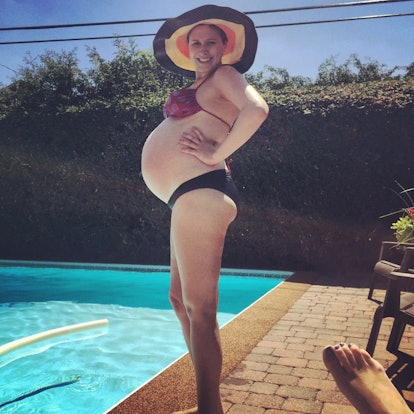 Pregnant Ceilidhe Wynn is standing next to a pool in her bikini and wears a hat