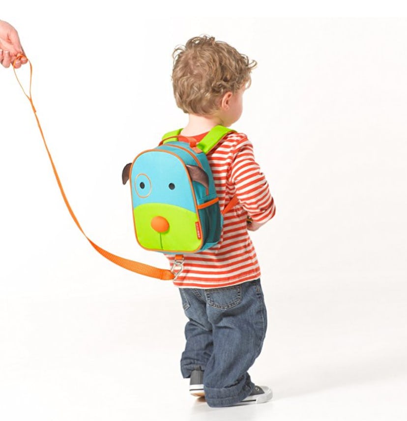 Little kid wearing a blue and green backpack that has an orange leash used for the child's safety