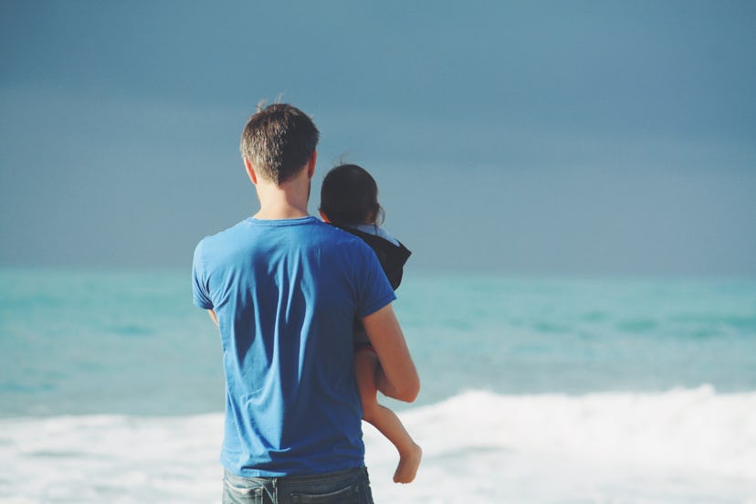 A father holding a baby while standing next to the sea