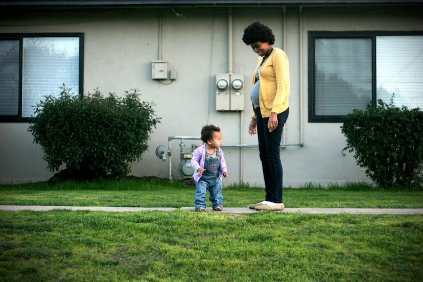 A pregnant woman standing in the garden next to her toddler 