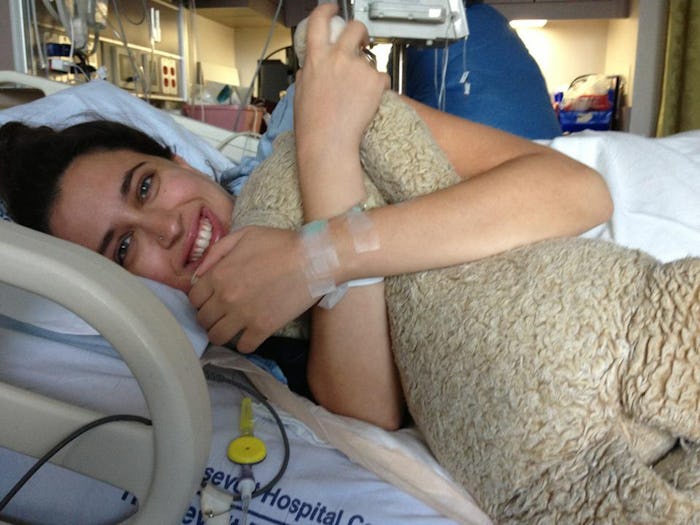 Mariah MacCarthy lying in a hospital bed after giving birth smiling and hugging a large teddy bear